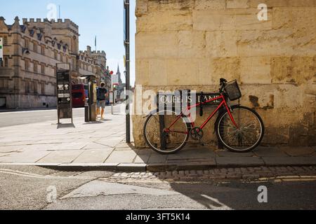 Vélo rouge appuyé contre un panneau de la rue Queens Lane sur un mur de grès ensoleillé dans une ville animée, des bâtiments historiques bordent le quartier, un passant se dirige vers un Banque D'Images