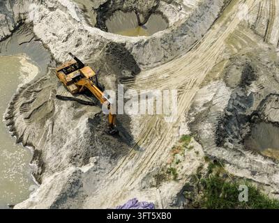 Vue aérienne d'une pelleteuse travaillant sur un site d'extraction de sable avec des fosses profondes, de l'eau boueuse et des traces de pneus à Dhaka, Division de Dhaka, Bangladesh. Banque D'Images
