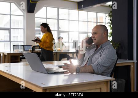 Divers collègues discutant et travaillant dans un open space, utilisant un ordinateur portable, un smartphone, une tablette, espace de copie Banque D'Images