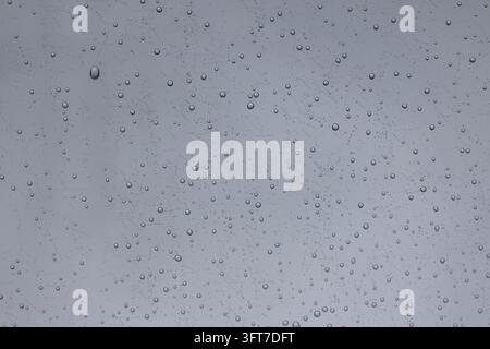 Texture de gouttes de pluie claires éparpillées sur du verre de fenêtre contre un ciel nuageux Banque D'Images