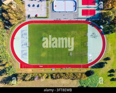 Vue aérienne du stade de l'école secondaire de Krimulda présentant un terrain de football vert, une piste de course rouge et des terrains de basket colorés à Ragana, Sigu Banque D'Images