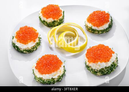 Cinq hors-d'œuvre festifs garnis de roe de saumon orange et d'aneth frais, disposés sur une assiette blanche avec une pelure de citron décorative. Banque D'Images
