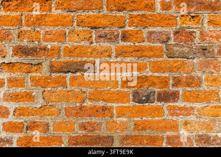 Close-up d'une maçonnerie rouge et orange érodée avec des surfaces rugueuses, des bords ébréchés et des joints de mortier pâles formant un fond mural texturé. Banque D'Images