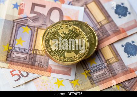 Pièces de cryptomonnaie physiques en or Bitcoin posées sur un fond de billets de cinquante euros en papier Banque D'Images