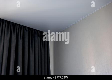 Coin intérieur minimaliste montrant des rideaux noirs du sol au plafond, un mur texturé gris clair et un plafond gris avec une moulure de couronnement. Banque D'Images