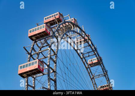 Cabines rouges en forme de gondole sur la grande roue de 1897 du parc d'attractions Wurstelprater, en Autriche, vues d'en bas contre un ciel automnal clair. Banque D'Images