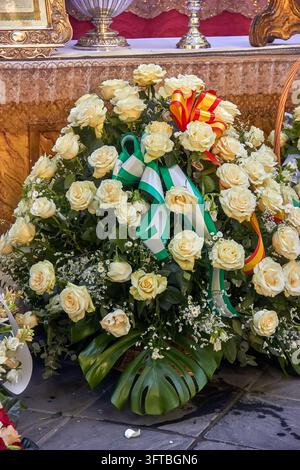 Un grand hommage de roses à la crème et de verdure avec des rubans verts, blancs, rouges et jaunes est exposé sous une table lors de l'offrande de fleurs. Banque D'Images