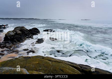 VUE ÉTENDUE D'UNE CÔTE SCANDINAVE GÉLÉE, ÎLE FINLANDAISE ÉLOIGNÉE EN HIVER PROFOND, UTÖ, FINLANDE : Une vue vaste et expansive montre une côte escarpée et rocheuse partiellement recouverte de neige et de grands amas de glace de mer sous un ciel gris et couvert. INFO : Utö est une île finlandaise éloignée dans la mer des Archipels, au sud de Turku. Connue pour son phare historique, ses paysages côtiers accidentés et son héritage maritime, c'est l'île habitée la plus méridionale de Finlande, attirant les visiteurs en quête de tranquillité, d'observation des oiseaux et de paysages spectaculaires de la mer Baltique. Banque D'Images