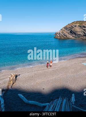 La plage de La Frana en Sardaigne, Italie, présente des eaux turquoise et une atmosphère sereine. Deux visiteurs profitent d'une promenade paisible le long du rivage sablonneux Banque D'Images