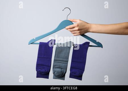 Main féminine tenant un cintre avec des chaussettes sur fond gris clair Banque D'Images