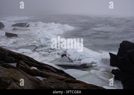BROKEN ICE ON A MISTY SHORE, REMOTE FINNISH ISLAND IN DEEP WINTER, UTÖ, FINLANDE : De gros morceaux de glace brisée s’entassent contre une côte sombre et rocheuse, la mer et l’horizon étant obscurcis par un épais brouillard. INFO : Utö est une île finlandaise isolée dans la mer archipélagique, au sud de Turku. Connue pour son phare historique, ses paysages côtiers accidentés et son héritage maritime, c’est l’île habitée la plus méridionale de Finlande, attirant les visiteurs en quête de tranquillité, d’observation des oiseaux et de paysages spectaculaires de la mer Baltique. Banque D'Images