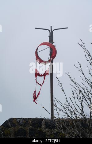 MOUFLE ROUGE DÉTRUIT ET DÉCHIRÉ, ÎLE FINNOISE ÉLOIGNÉE EN HIVER PROFOND, UTÖ, FINLANDE : Une vue rapprochée montre une manche à vent rouge complètement déchirée et en lambeaux suspendue à son cadre contre un ciel gris. INFO : Utö est une île finlandaise éloignée dans la mer des Archipels, au sud de Turku. Connue pour son phare historique, ses paysages côtiers accidentés et son héritage maritime, c'est la plus méridionale des îles habitées de Finlande, attirant les visiteurs en quête de tranquillité, d'observation des oiseaux et de paysages spectaculaires de la mer Baltique. Banque D'Images