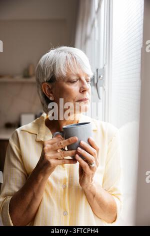 Sénior femme se détendant les yeux fermés, tenant une tasse de café, profitant d'un moment de paix Banque D'Images