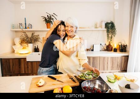 Mère et fille heureuses s'embrassant dans la cuisine en préparant une salade saine Banque D'Images