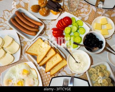 Petit-déjeuner copieux et appétissant dans un hôtel géorgien comprenant des œufs au plat, des boulettes, du fromage, du beurre, des saucisses, des légumes, des olives, du pain et des pâtisseries sucrées Banque D'Images
