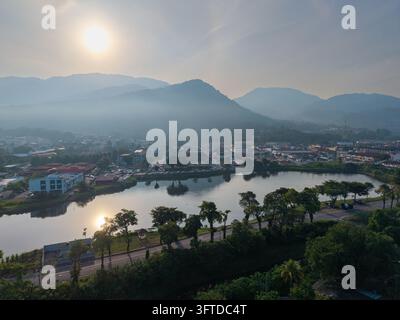 Le soleil doré brille au-dessus d'une chaîne de montagnes brumeuses. Le lac reflète le ciel et les collines lointaines avec une clarté calme à Kampar, Perak Banque D'Images