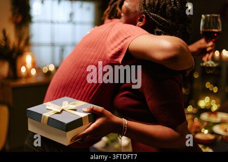 Homme noir tenant une boîte-cadeau surprise et embrassant une femme noire au dîner Banque D'Images
