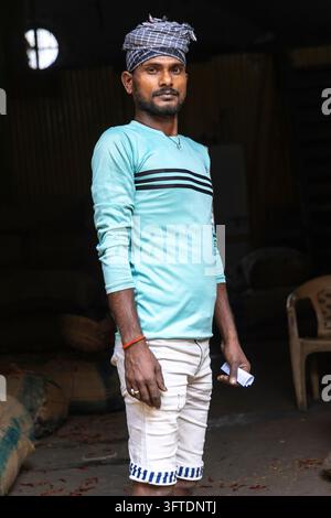 Portrait d'un jeune ouvrier tenant un petit papier dans sa main avec des sacs empilés dans l'espace sombre derrière lui, Bengale occidentale, Howrah, Inde Banque D'Images