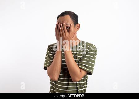 Jeune homme beau sur fond blanc isolé, couvrant les yeux et regardant à travers les doigts Banque D'Images
