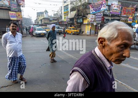 Scène de rue en grand angle avec un homme aux cheveux blancs de profil et des hommes traversant une intersection avec des panneaux et des taxis, Bengale occidentale, Kolkata, Inde Banque D'Images
