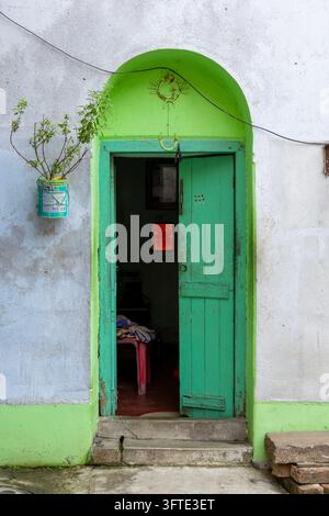 Arc peint en vert vif autour d'une porte en bois entrouverte dans un mur pâle avec une petite plante dans une boîte en fer-blanc, Bengale occidentale, Kolkata, Inde Banque D'Images