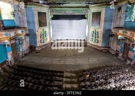 Vue large d'un théâtre abandonné avec des murs bleus et turquoise, un écran blanc vierge et des rangées de sièges en bois poussiéreux, Bengale occidentale, Kolkata, Inde Banque D'Images