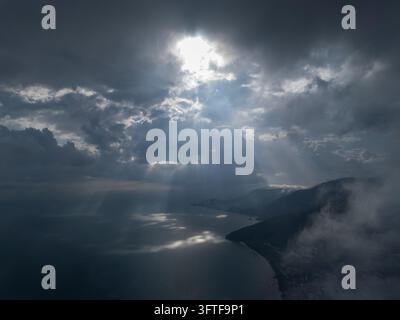 Les rayons de soleil percent les nuages sombres au-dessus des eaux brumeuses. Les crêtes des montagnes s'estompent dans le brouillard en dessous à Teluk Bahang Banque D'Images