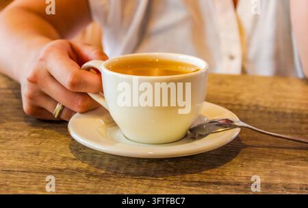 Main tenant une tasse de thé blanche à une table en bois pour des concepts de café cosy et d'hospitalité Banque D'Images