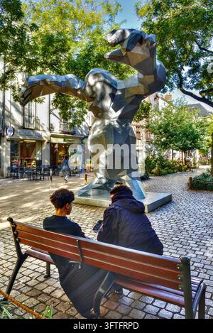 Deux jeunes hommes assis sur un banc regardant un smartphone, surplombés par la sculpture Le Monstre de Xavier Veilhan - Tours, Indre-et-Loire (37), France. Banque D'Images