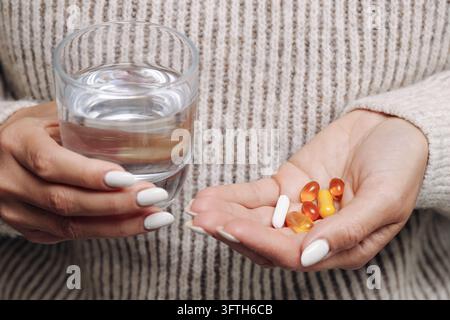 Femme tenant un verre d'eau et des capsules de vitamines colorées dans la paume de sa main. Arrière-plan sur les soins de santé pour les compléments alimentaires, les médicaments quotidiens et la santé. Banque D'Images
