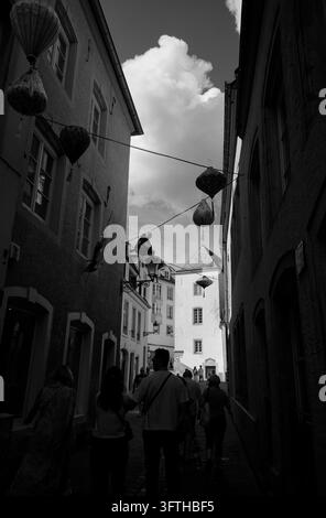 Des lanternes pendent au-dessus d'une ruelle ombragée de la vieille ville tandis que des visiteurs en silhouette marchent vers une tour baignée de soleil dans la ville de Luxembourg Banque D'Images
