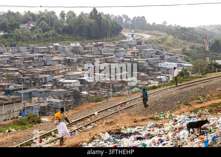 Femme et garçon avec un ballon orange marchant le long d'une voie ferrée au-dessus de la zone de Kibera avec des maisons en tôle ondulée, Comté de Nairobi, Nairobi, Kenya Banque D'Images