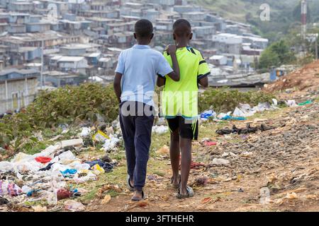 Deux garçons marchant bras dessus bras dessous sur un chemin avec des ordures au-dessus de la zone de Kibera, Nairobi County, Nairobi, Kenya Banque D'Images