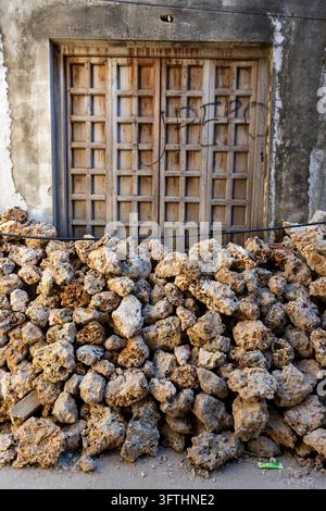 tas de gros blocs de pierre de corail empilés devant une vieille porte en bois lambrissée avec des graffitis dans un mur gris usé, Stone Town, Tanzanie Banque D'Images
