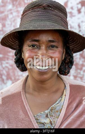 Un homme âgé portant un chapeau en feutre vert sourit doucement devant un mur érodé, Ihorombe, Ranohira, Madagascar Banque D'Images
