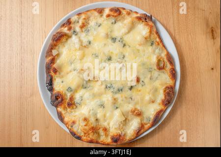 Pizza italienne quattro formaggi garnie d'un mélange de fromages fondus, avec une croûte dorée, servie sur une assiette blanche sur une table en bois. Banque D'Images