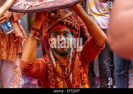 Homme barbu portant un turban orné regarde anxieusement sous un bouclier en cuir à Lathmar Holi, Uttar Pradesh, Barsana, Inde Banque D'Images