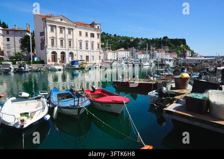 Petits bateaux de pêche amarrés dans le port intérieur de Piran, en Slovénie, avec le musée maritime Sergej Mašera et l’horizon urbain en arrière-plan. Banque D'Images