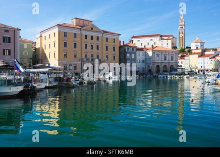 Havre turquoise serein de Piran, Slovénie, reflétant les bâtiments côtiers colorés, le musée Sergej Mašera et l'église Saint-Georges. Banque D'Images