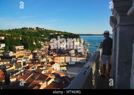 Touriste regardant depuis le clocher de Saint-Georges sur les toits aux tuiles rouges, la place Tartini et le port de Piran, en Slovénie. Banque D'Images