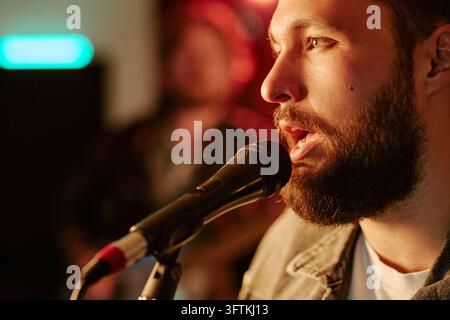 Homme barbu chantant dans un microphone pendant une performance de concert en direct Banque D'Images