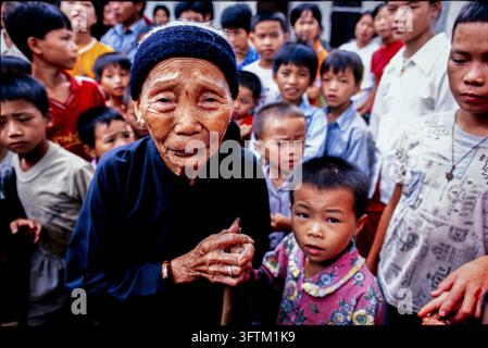 Une femme âgée tenant une canne se tient au milieu d'un groupe d'enfants attentifs dans une communauté en Chine. Banque D'Images