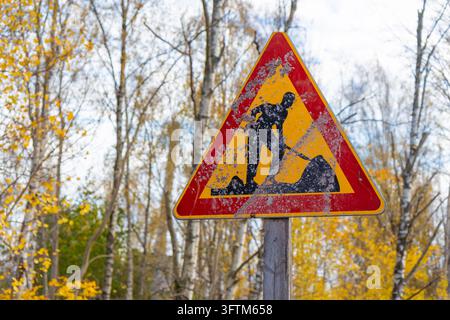 Un panneau triangulaire usé et sale des travaux routiers se dresse le long d'une route à Espoo, en Finlande, représentant une silhouette noire d'un ouvrier avec une pelle sur le Banque D'Images