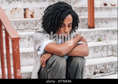 Jeune homme noir assis sur des marches, l'air triste, se sentant seul et stressé Banque D'Images