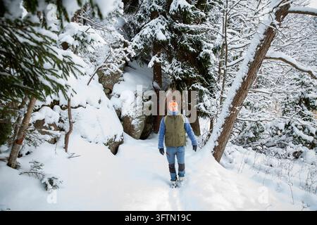 Un randonneur marche le long d'un sentier forestier enneigé à côté d'une paroi de granit, une aventure hivernale active dans la nature finlandaise immaculée Banque D'Images