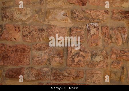 Vue rapprochée d'un mur de briques irrégulier avec une maçonnerie brun rougeâtre, un mortier irrégulier et des surfaces fortement érodées. Le motif horizontal répétitif a Banque D'Images