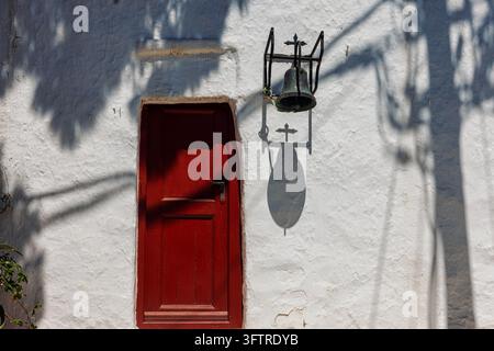 Une chapelle traditionnelle blanchie's à la chaux avec des portes rouges distinctives et une architecture cycladique simple se dresse sous un ciel bleu clair sur l'île de Mykonos dans le Banque D'Images