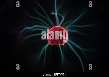 Grossissement d'un globe à plasma lumineux présentant un centre rouge vif émettant des filaments de gaz ionisé bleu électrique et cyan sur un fond noir Banque D'Images