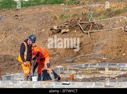 Salopette orange et casque de sécurité portés par des ouvriers du bâtiment creusant près des fondations d'un bâtiment sur le chantier Banque D'Images