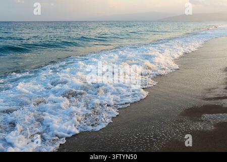 Vague de mer avec une mousse blanche roulant sur le rivage sablonneux Banque D'Images